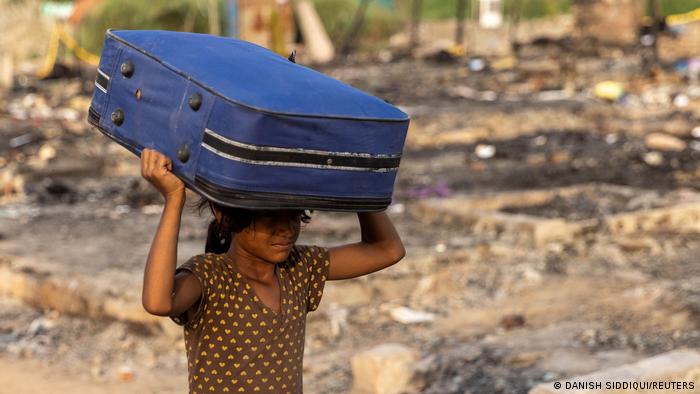 A Rohingya refugee carries her belongings to a temporary shelter after a fire destroyed a Rohingya refugee camp 