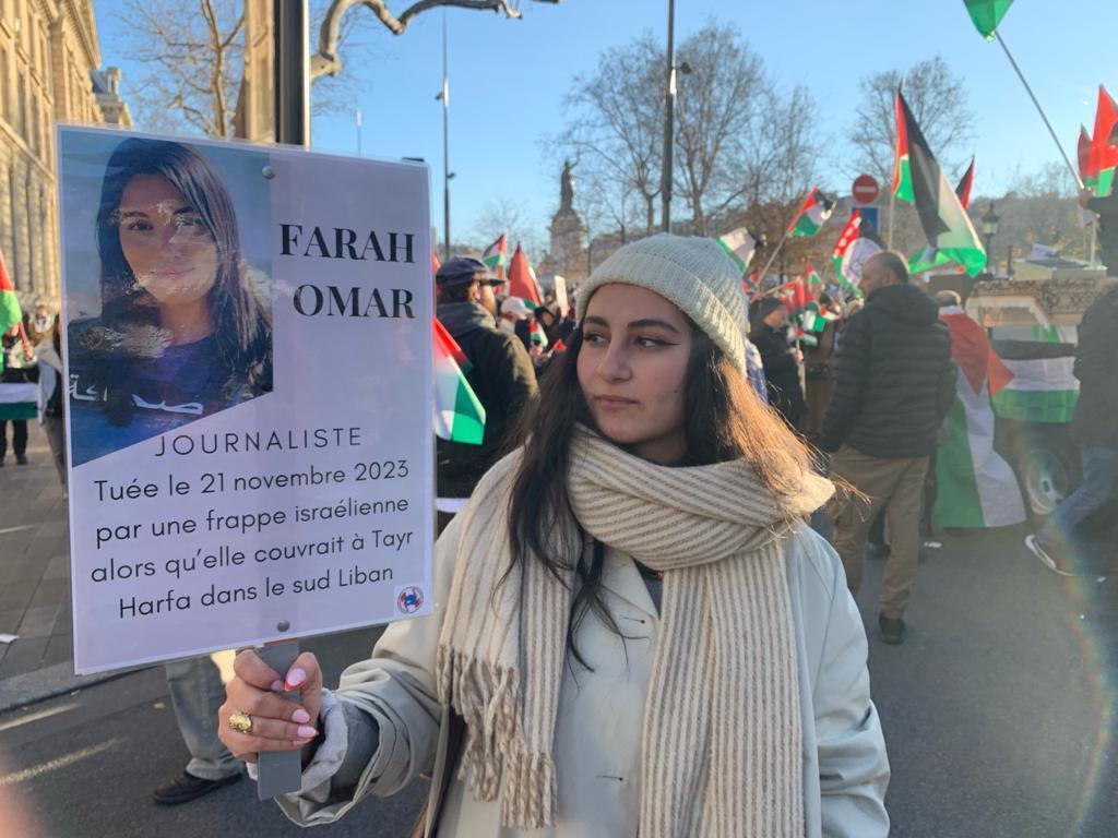 صحافية تشارك في مظاهرة مؤيدة للفلسطينيين في باريس يوم الأحد 17 ديسمبر/كانون الأول تحمل ملصقا عليه صورة فرح عمر، مراسلة قناة الميادين التلفزيونية، التي قُتلت جراء إطلاق صاروخ بجنوب لبنان في 21 نوفمبر/تشرين الثاني 2023.